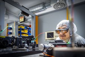 Ein Wissenschaftler mit Laserbrille und Haarnetz betrachtet einen optischen Versuchsaufbau.