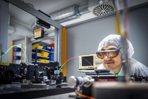 A scientist with laser googles and a hairnet examines an optical experimental setup.