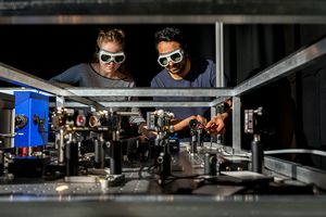 Eine junge Wissenschaftlerin und ihr Kollege, die beide Laserschutzbrillen tragen, betrachten ein optisches Experiment.