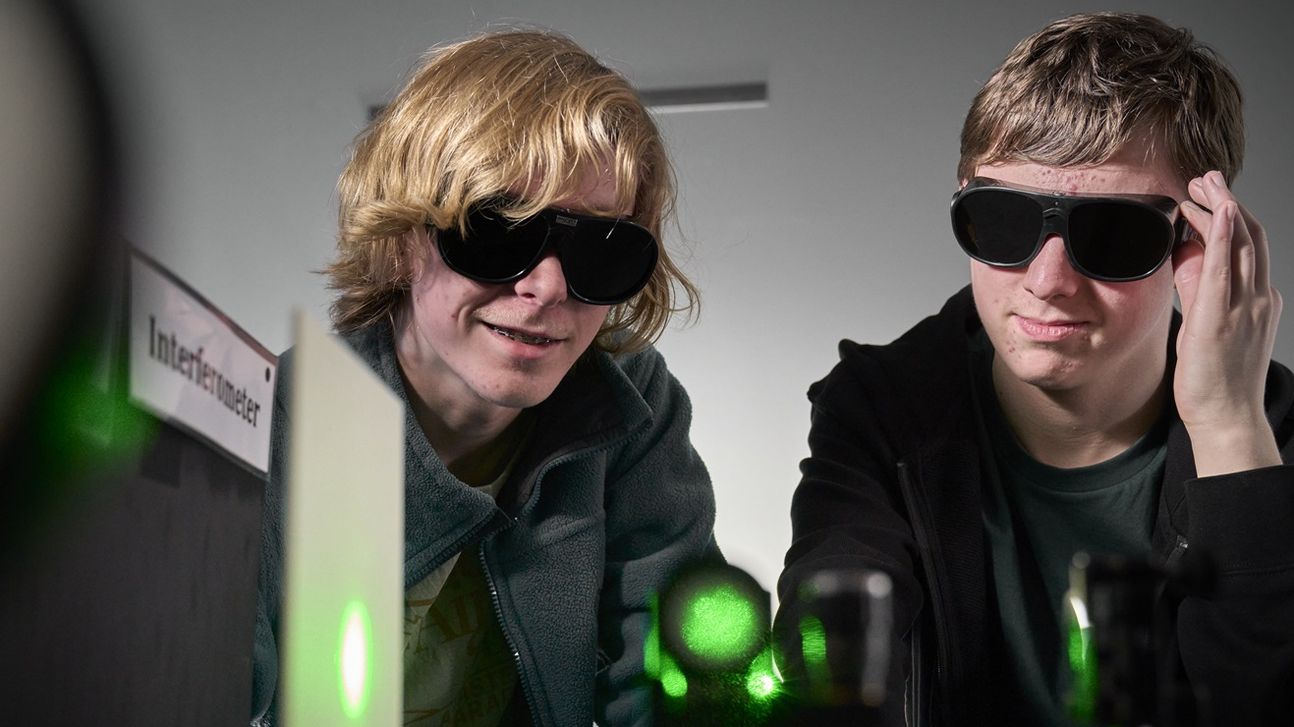 Two boys wearing protective goggles infront of an optical experiment with green lasers. 