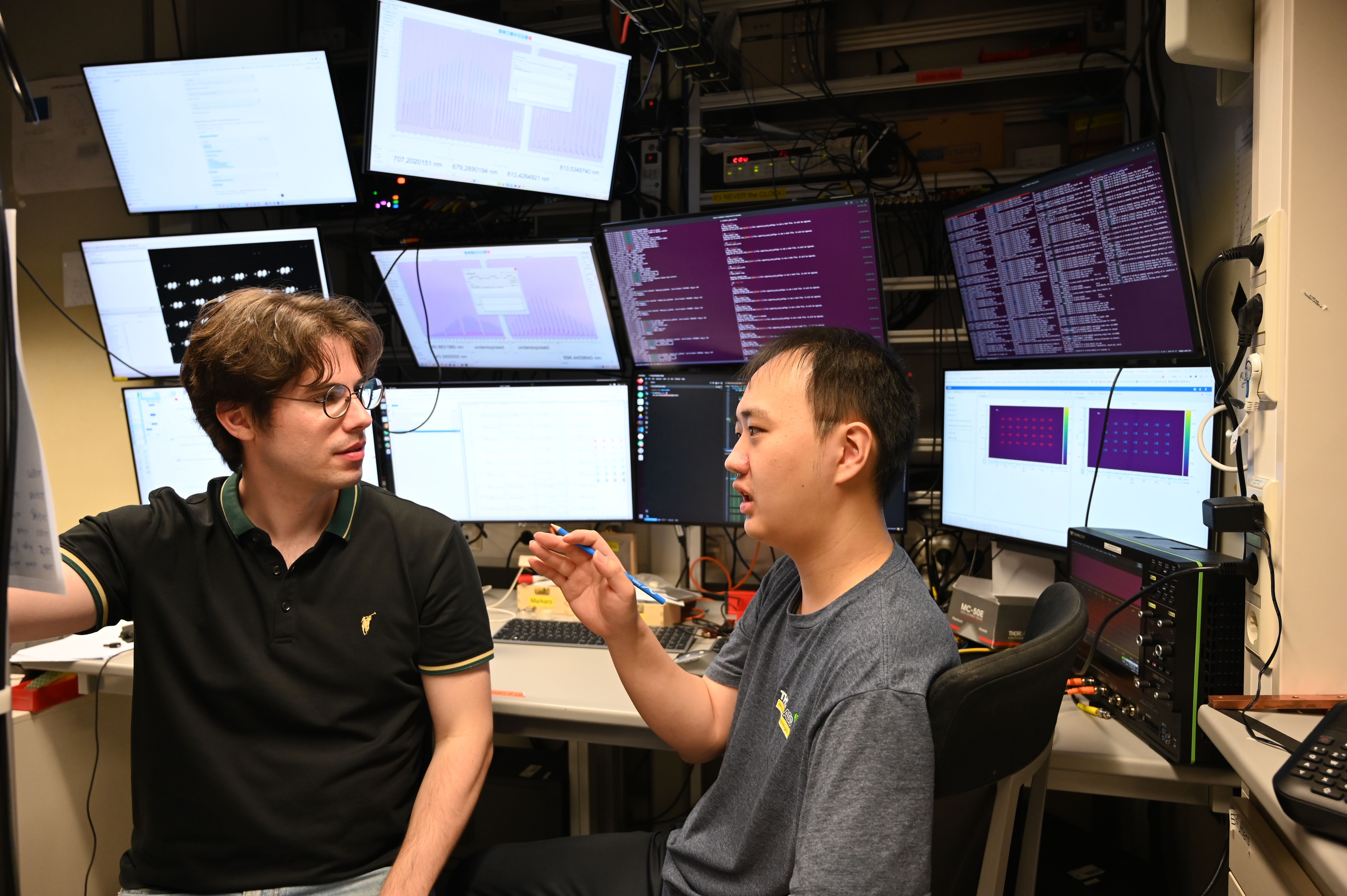 Physicist Dimitris Tsevas is talking to a colleague in the laboratory. In the background, numerous computer monitors can be seen.