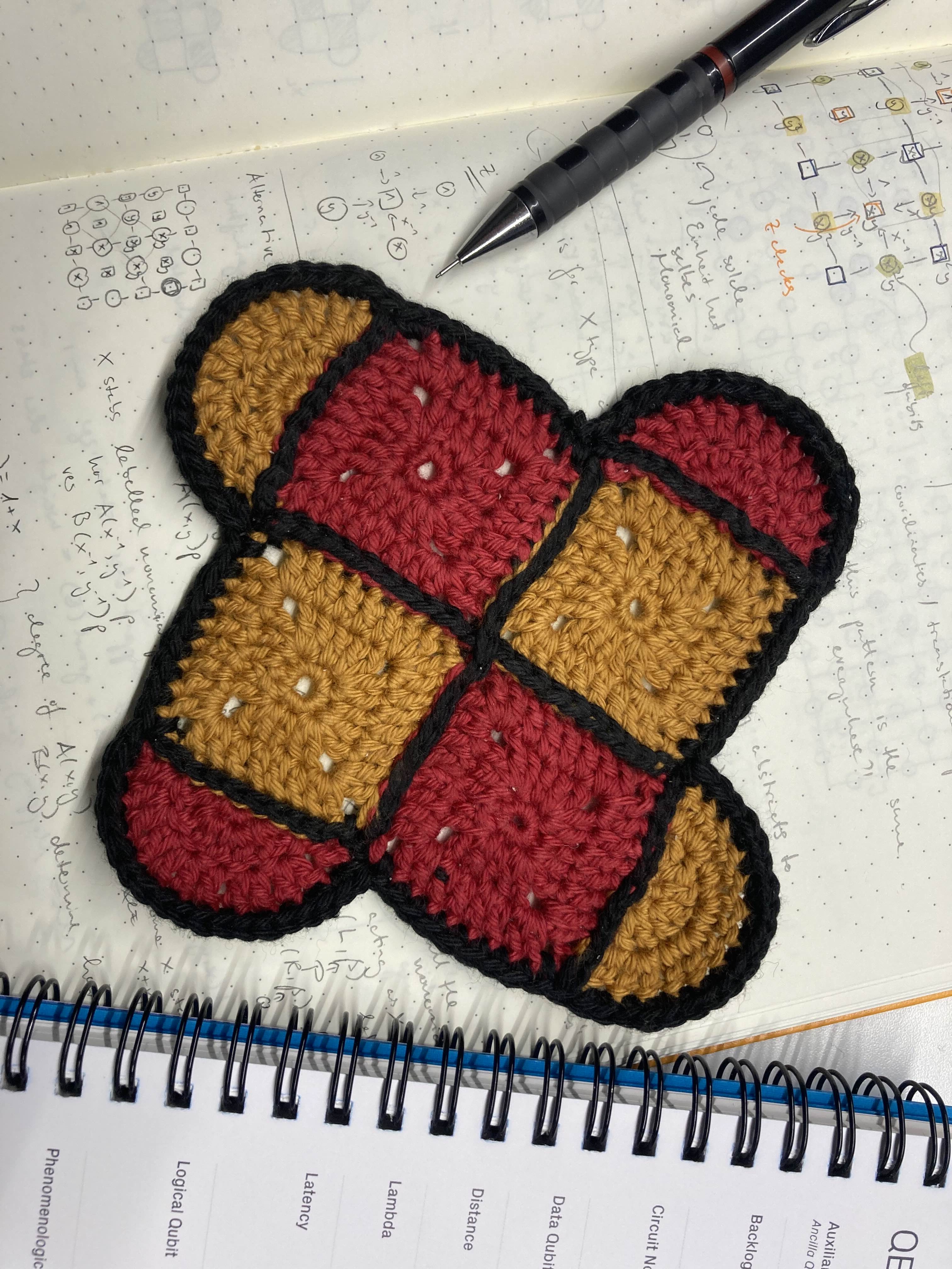 Laura Herzog's hand-crocheted coaster, which represents a Surface code. The crocheted square consists of two red and two yellow squares arranged in a checkerboard pattern. A semicircle, also red or yellow, is attached to each side along half the length of the side.